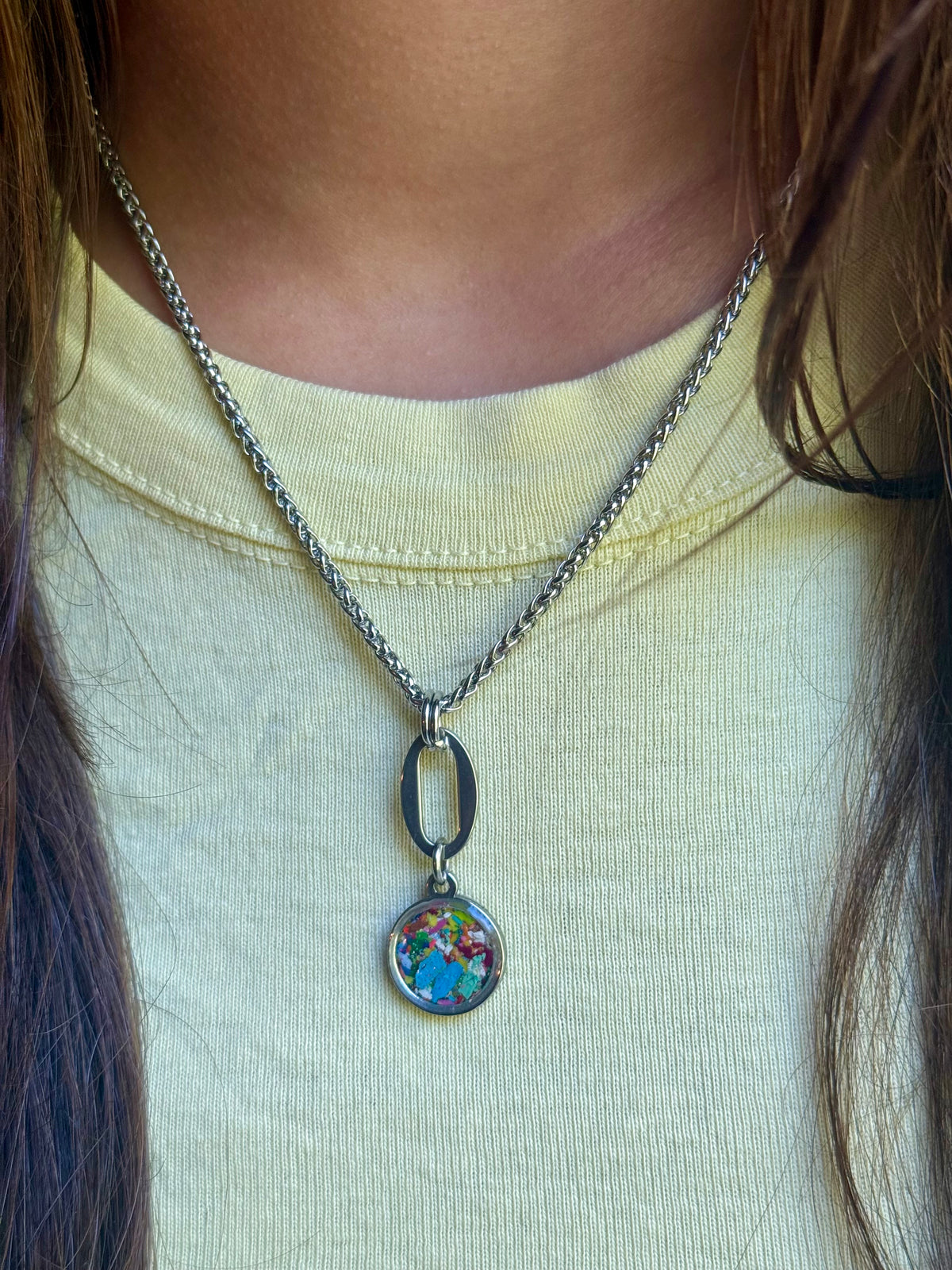 Model wearing the Marisol sky blue and multicolor resin pendant necklace on an 18-inch stainless steel chain, sitting flat below the collarbone