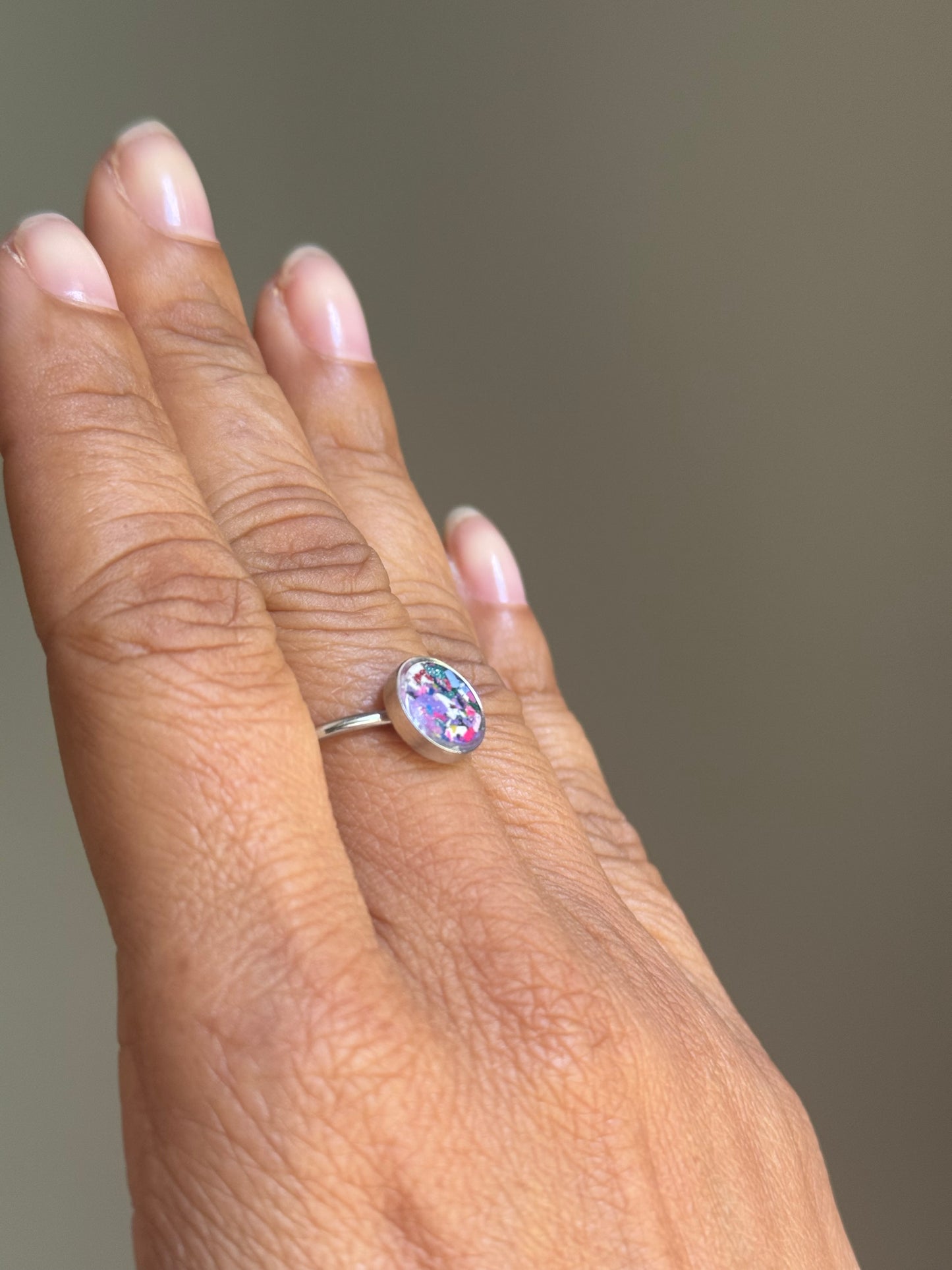 Close-up of a minimalist stainless steel ring showcasing a hand-placed, delicate mosaic of pastel purple crayon shavings.