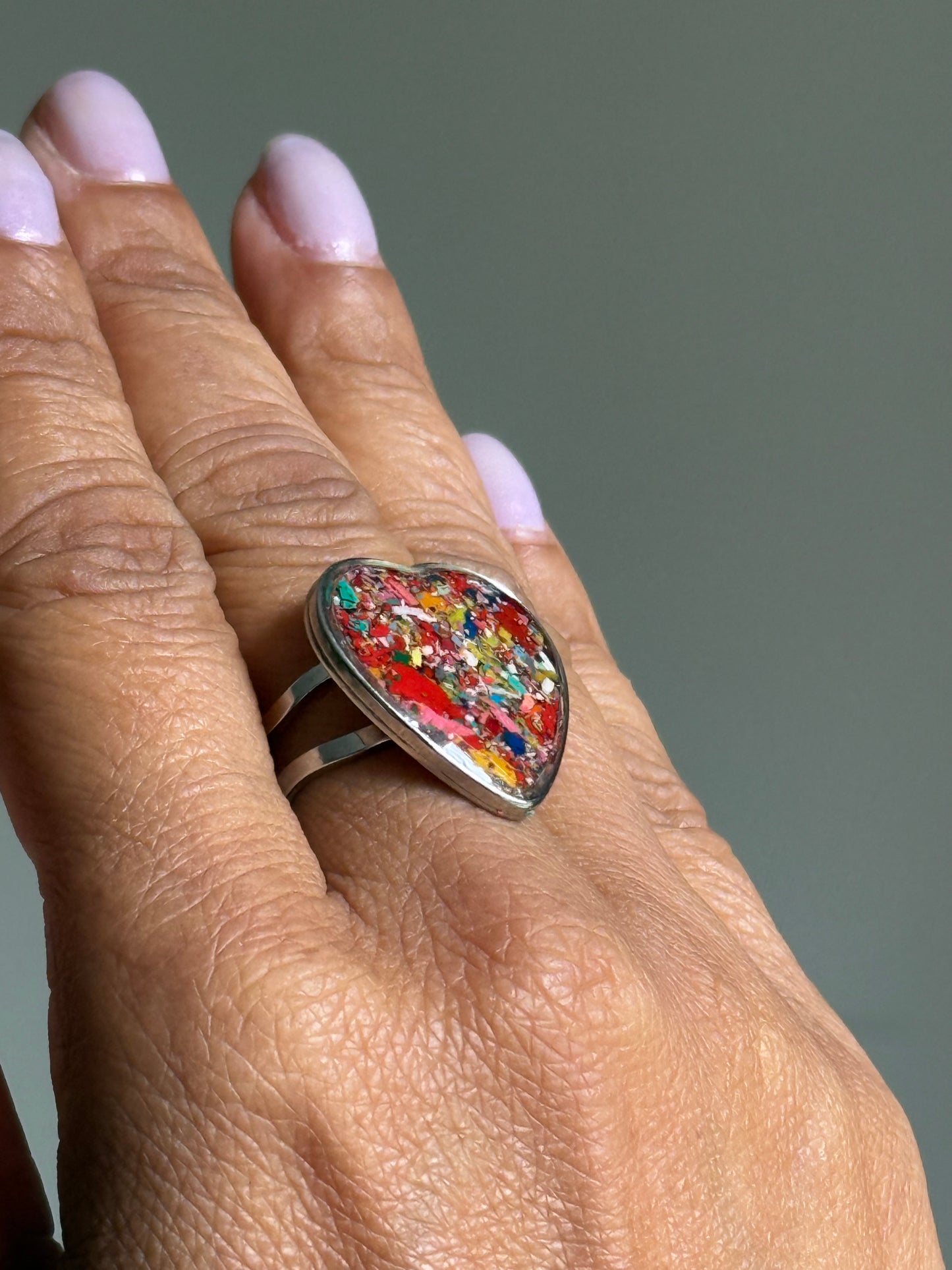 Handcrafted stainless steel crayon ring holding a bright red and multicolor crayon shavings. It's crayon jewelry. Heart shaped rings.