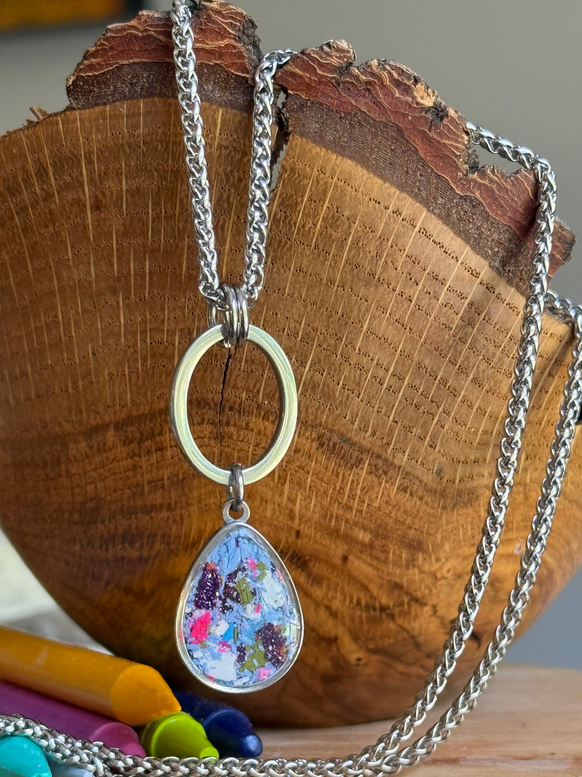 Side profile of the periwinkle crayon pendant hanging off a wooden bowl showing the stainless steel bezel setting.