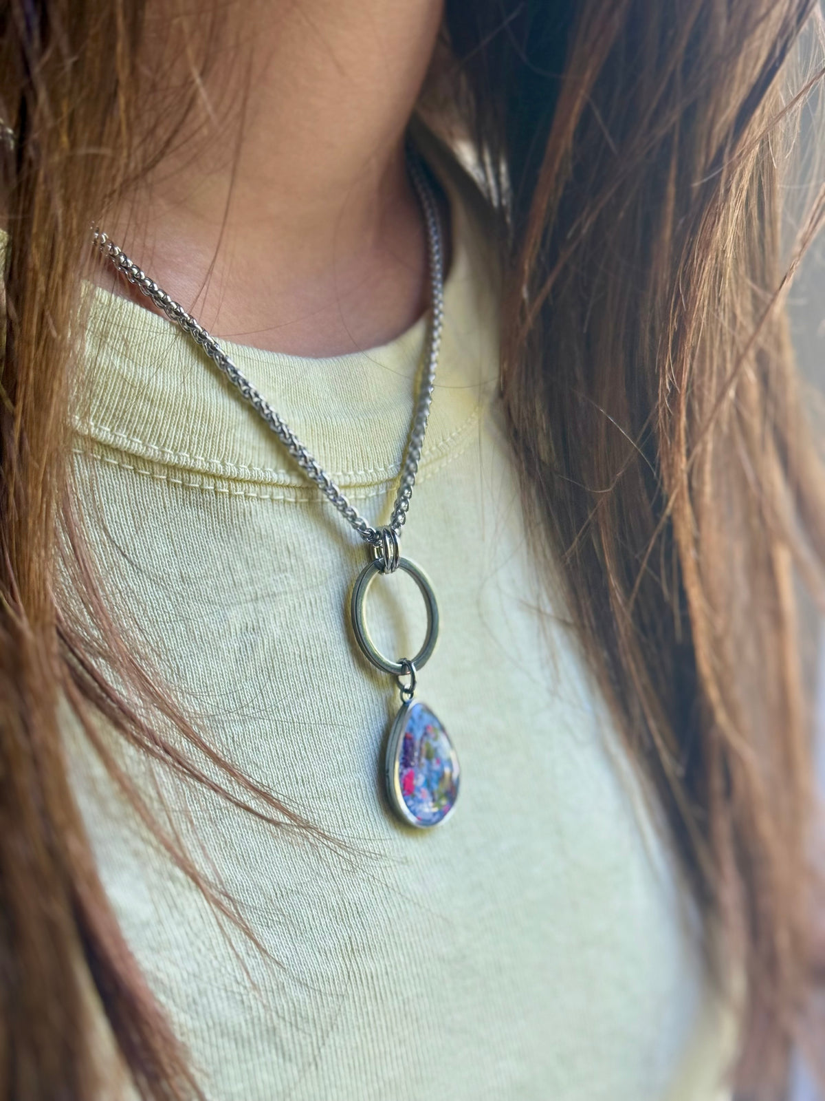 Model in a bright yellow top wearing the Carmen periwinkle pink resin pendant on a stainless steel chain