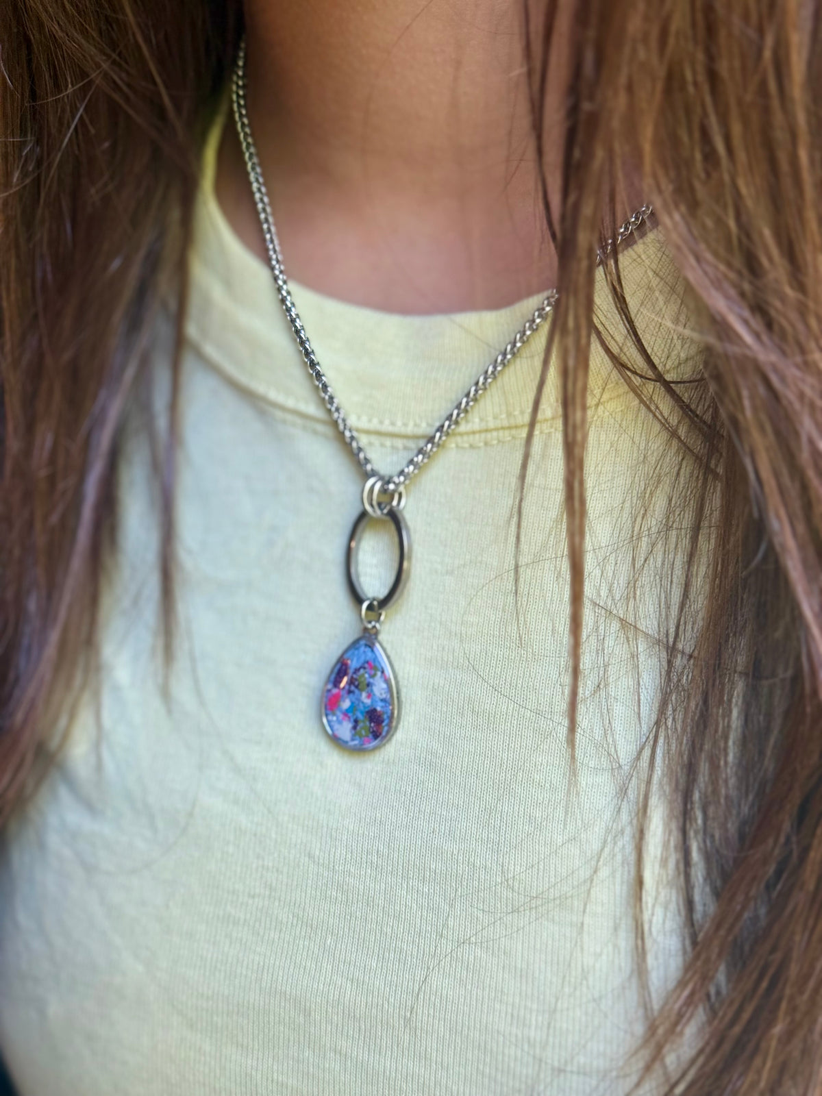 Close-up of model in a yellow top showcasing the Carmen pendant featuring dark purple, periwinkle, and hot pink resin inlay.