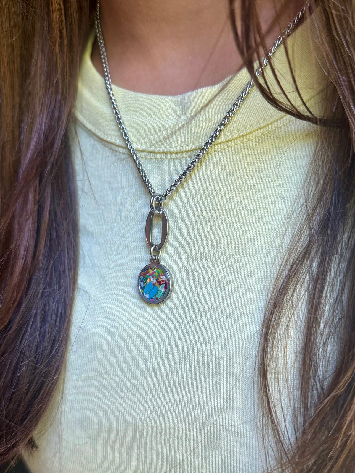 Close-up of model wearing the oval Marisol sky blue resin pendant necklace styled with a yellow top.