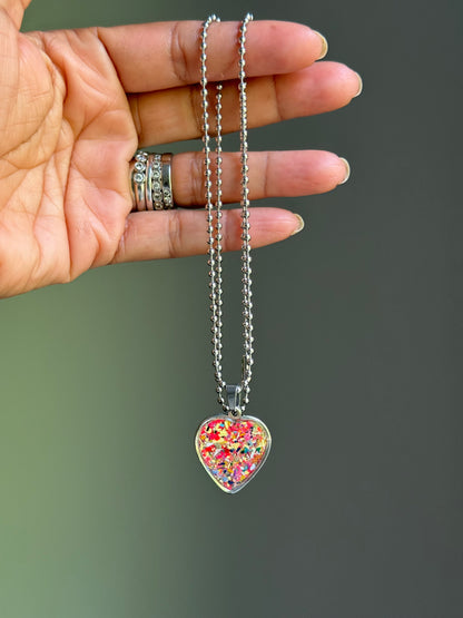 Solar Spark heart-shaped pendant displayed next to its gift-ready tin can and Crayonfetti jewelry bag.