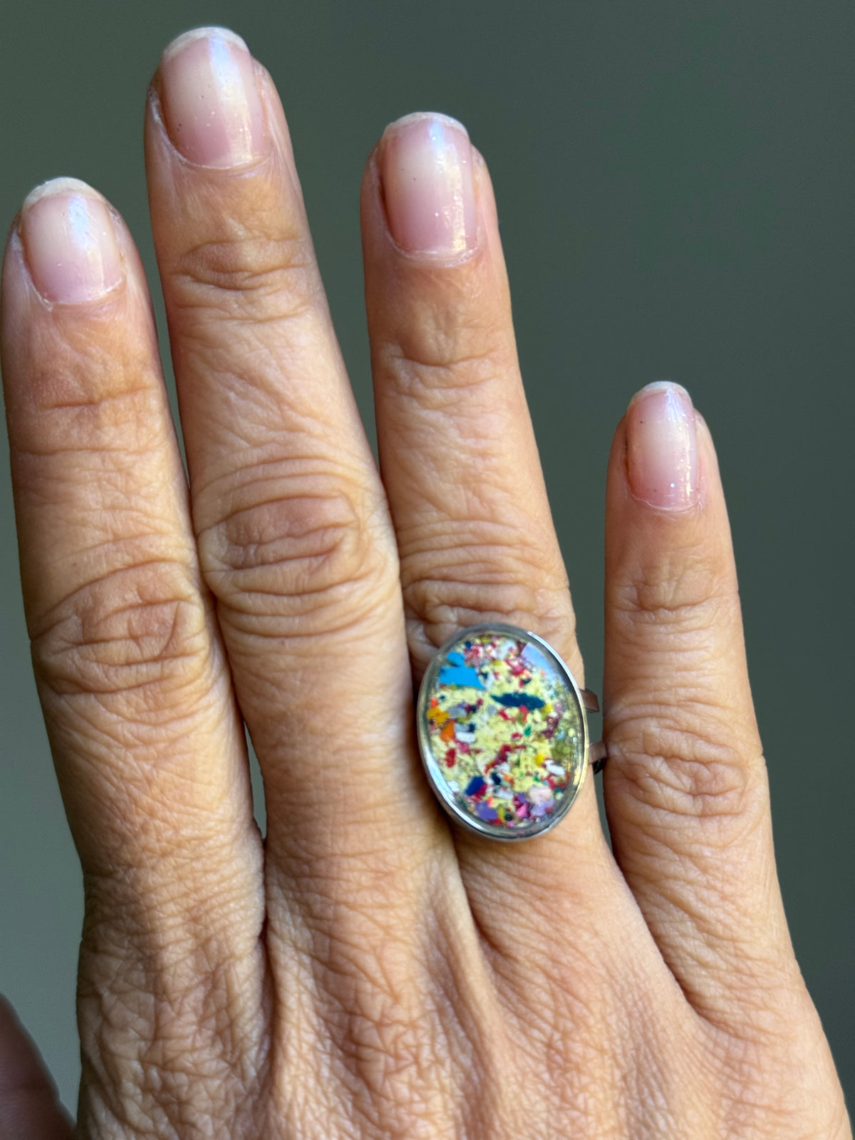 Close-up of oval statement ring with multi-color crayon shavings sealed under clear resin.