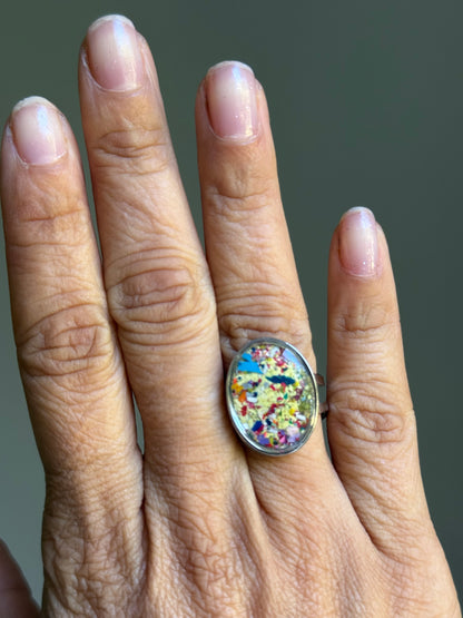 Close-up of oval statement ring with multi-color crayon shavings sealed under clear resin.