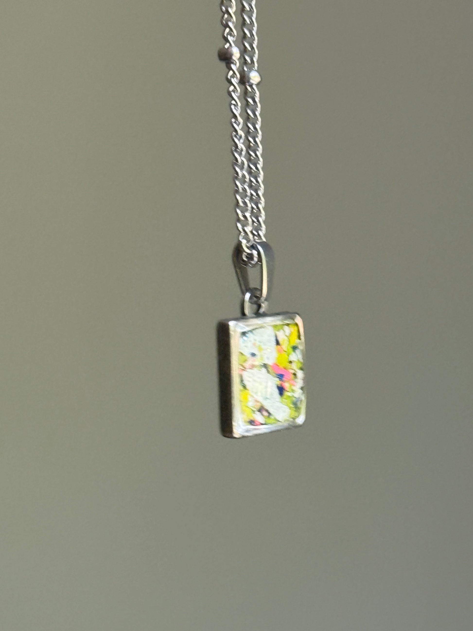 Square crayon jewelry pendant showcasing layered white, navy, and yellow crayon shavings sealed in clear resin by crayon jewelry shop crayonfetti