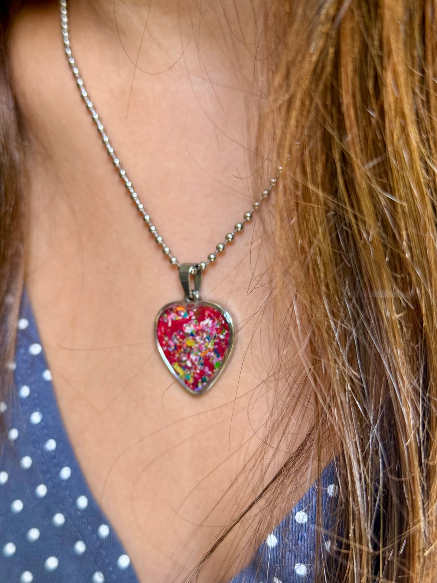 A close-up of a person wearing a heart-shaped pendant filled with multicolored crayons.  Crayon jewelry by crayonfetti