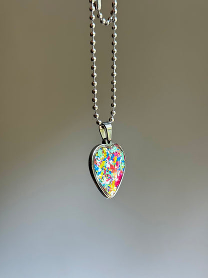 A stainless steel heart-shaped pendant necklace filled with multicolored crayon shavings.  Crayon jewelry bt Crayonfetti. By mother-daughter.