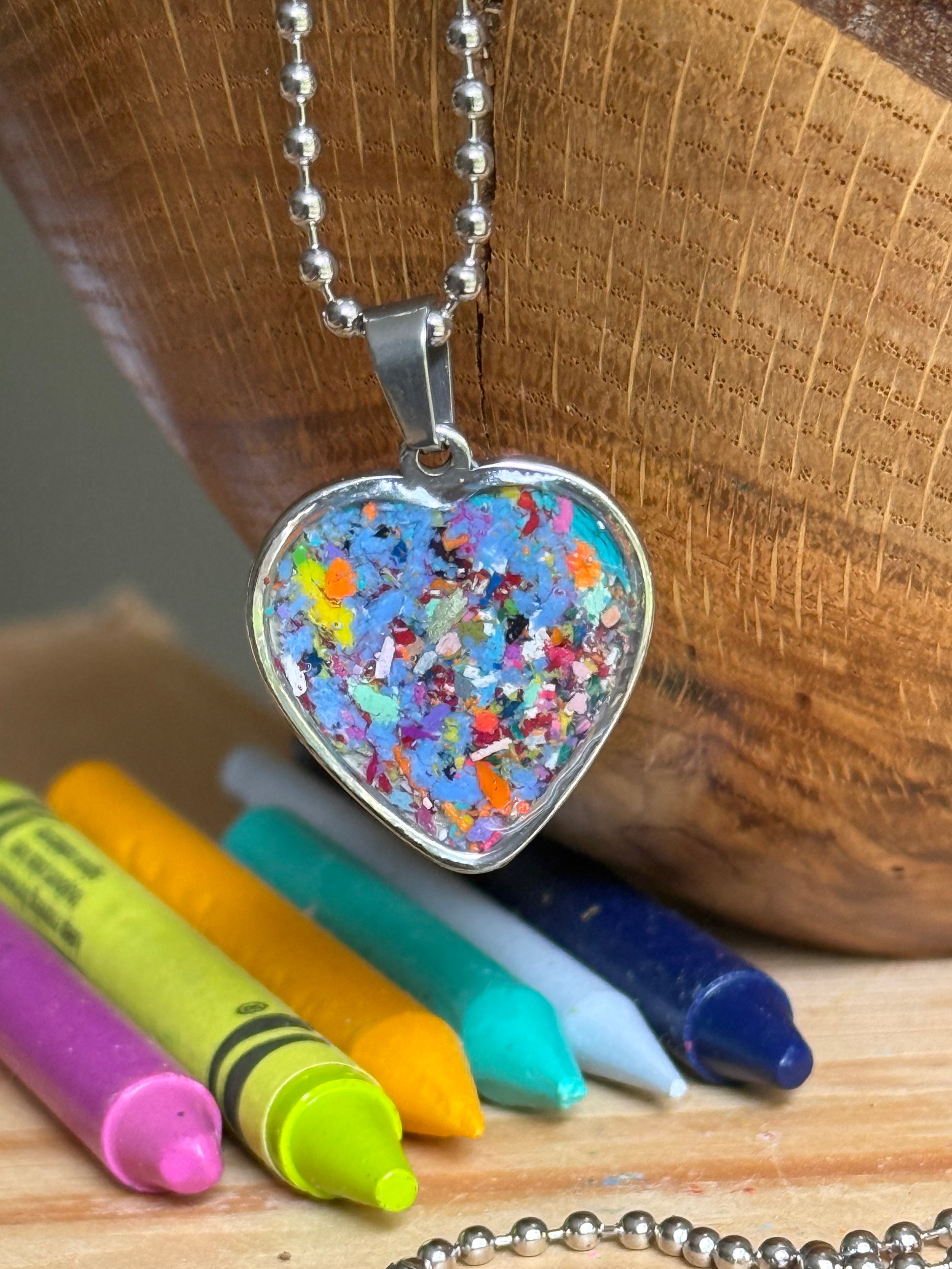 A heart-shaped pendant necklace filled with multicolored crayons, hanging from a silver ball chain. Crayon jewelry by crayonfetti