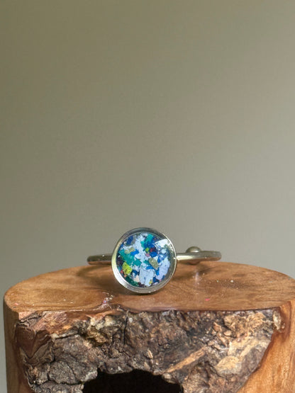 A dainty stainless steel ring featuring a deep, moody mosaic of dark blue and black crayon shavings, created as unique crayon jewelry by Crayonfetti.