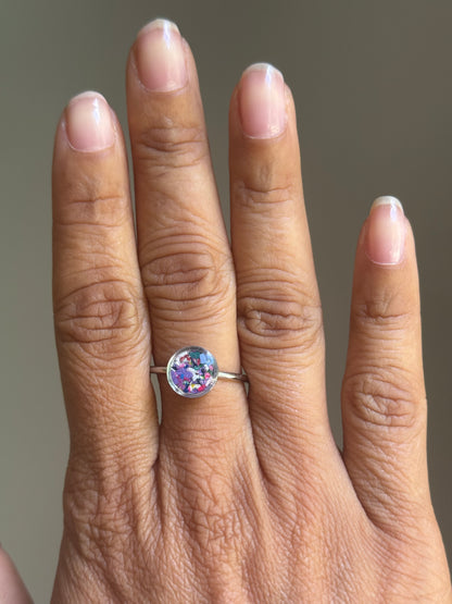 A person wearing a minimalist stainless steel Lavender Mist ring on their finger, styled as a dainty stacking ring alongside other colorful jewelry.