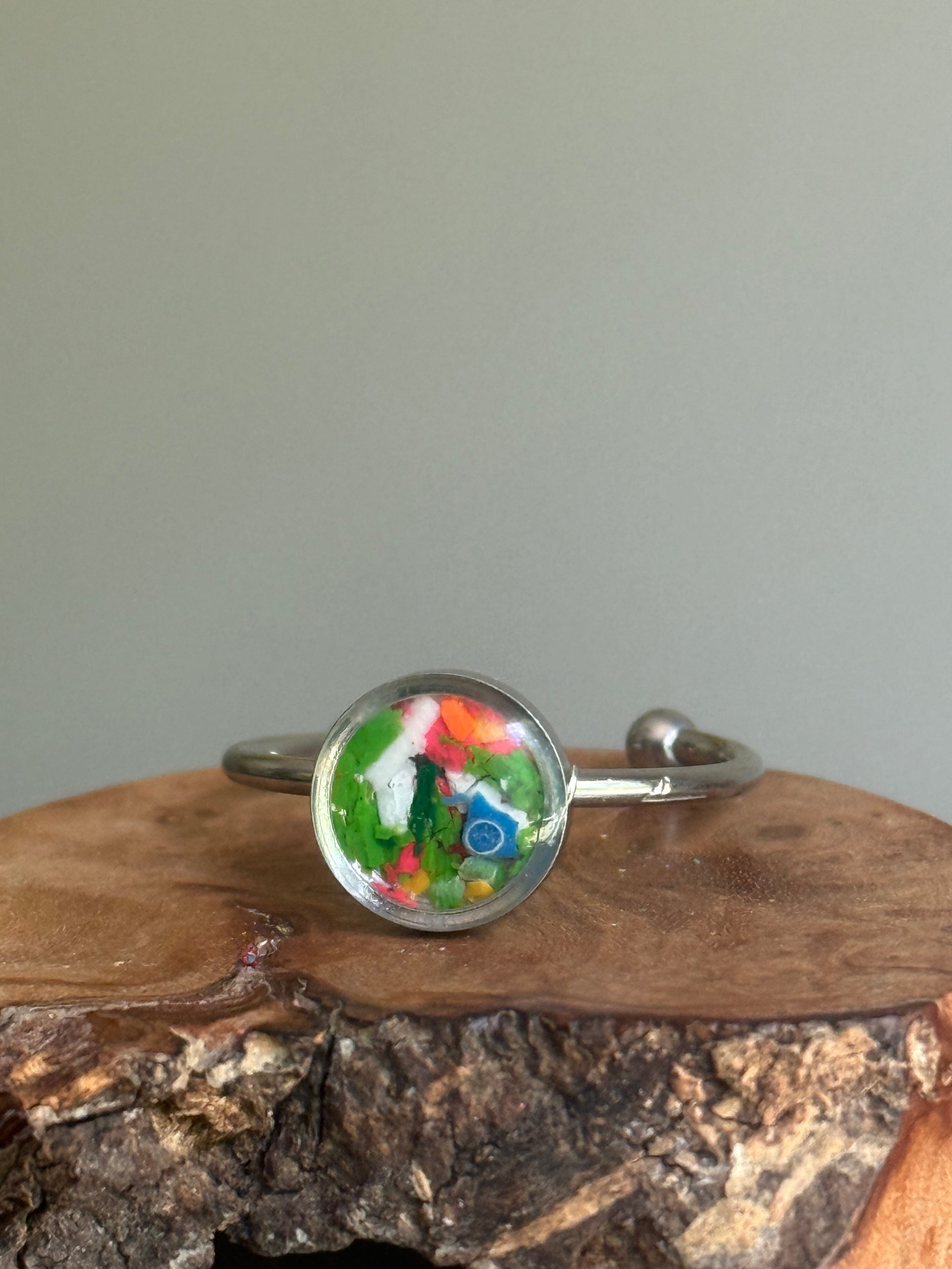 A dainty stainless steel ring featuring a bright, energetic burst of neon orange crayon shavings, created as unique crayon jewelry by Crayonfetti.
