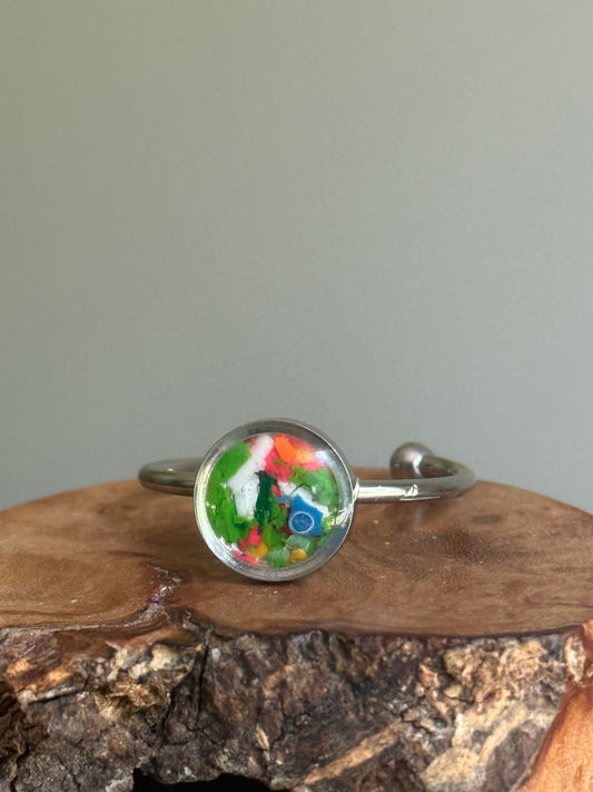 A dainty stainless steel ring featuring a bright, energetic burst of neon orange crayon shavings, created as unique crayon jewelry by Crayonfetti.