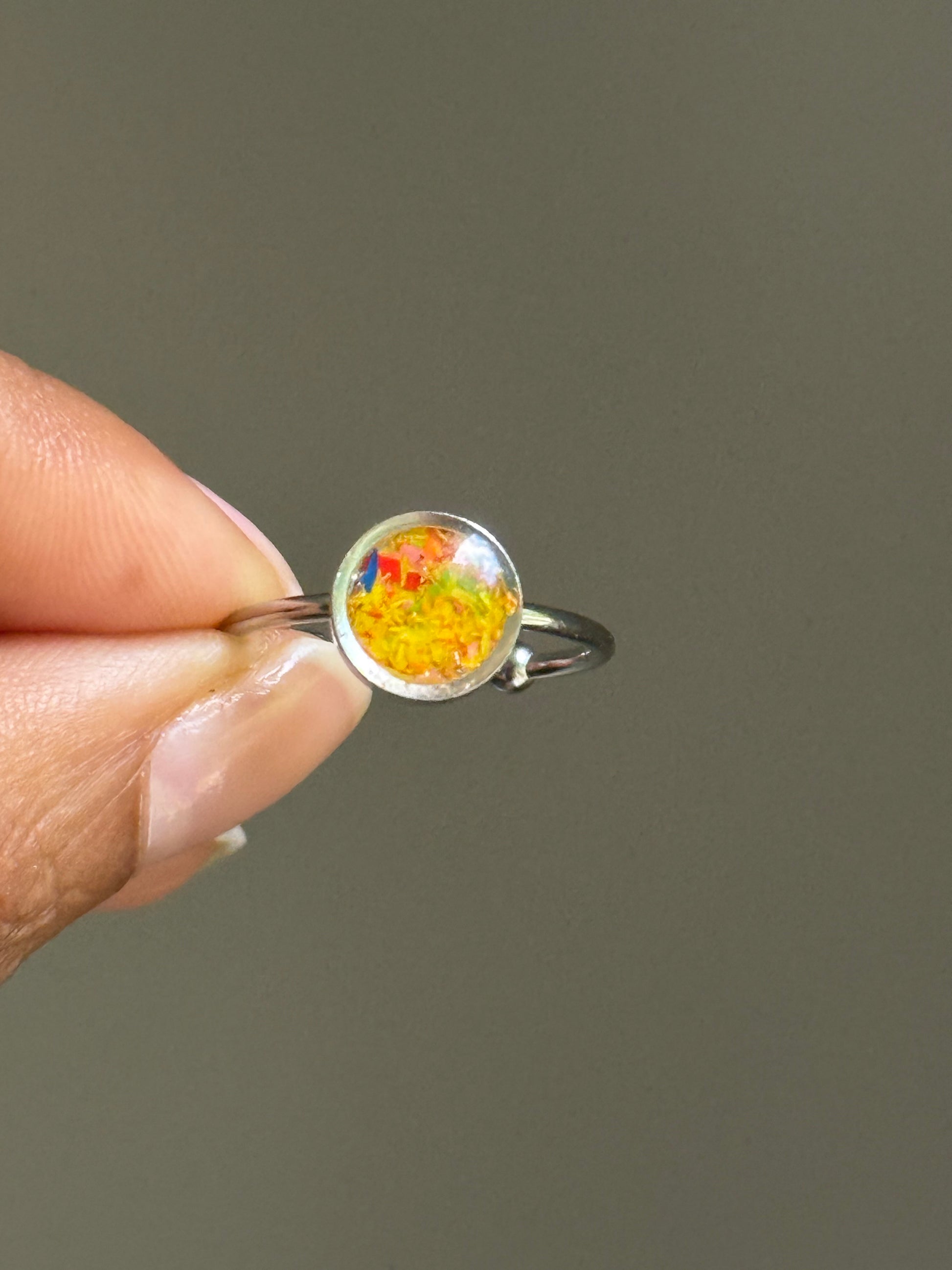 Close-up of a delicate stainless steel ring filled with a cheerful burst of marigold and yellow crayonfetti, creating a textured and colorful jewelry ring