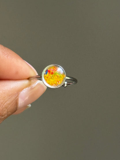 Close-up of a delicate stainless steel ring filled with a cheerful burst of marigold and yellow crayonfetti, creating a textured and colorful jewelry ring