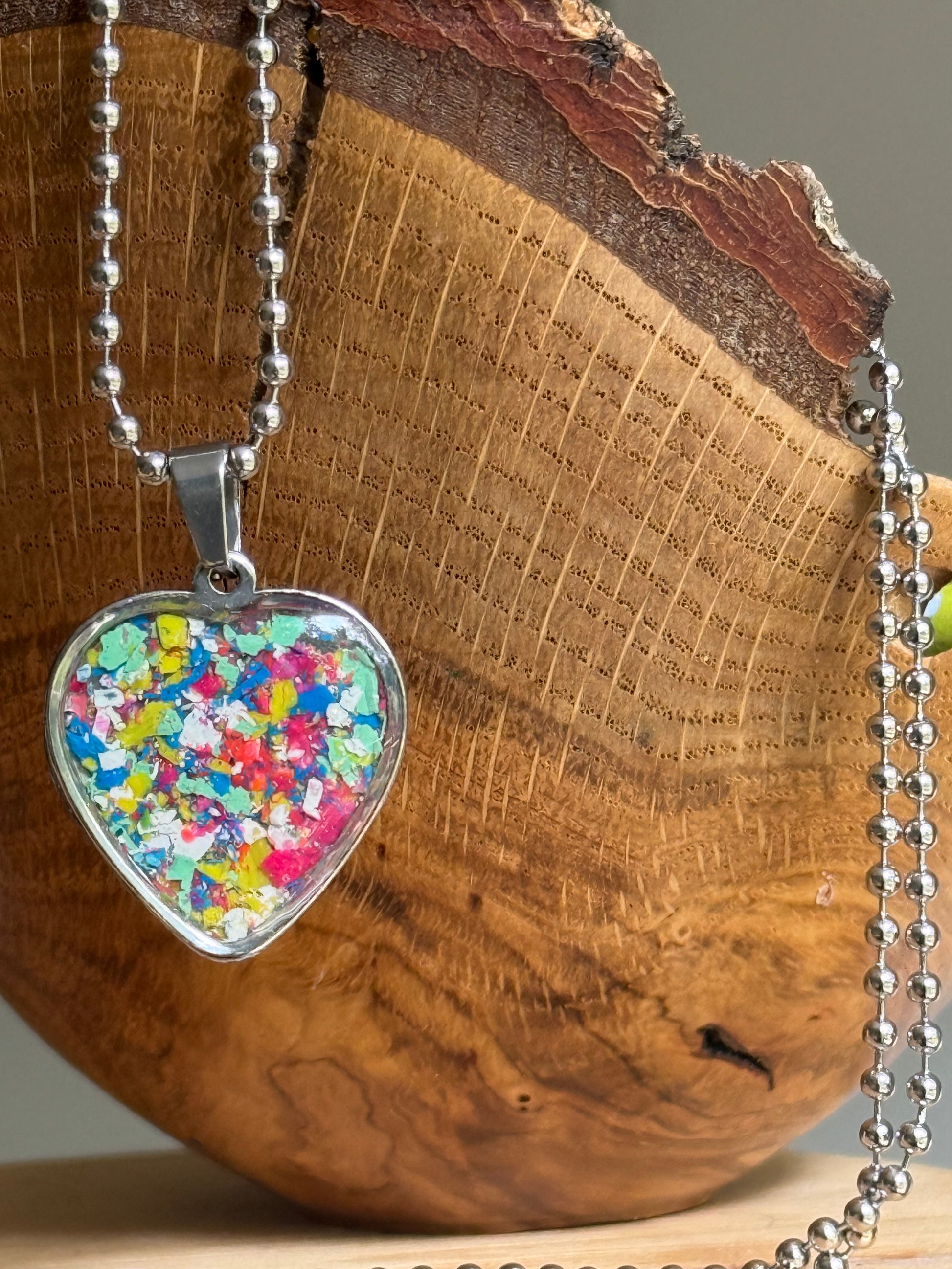 A stainless steel heart-shaped pendant necklace filled with multicolored crayon shavings.  Crayon jewelry bt Crayonfetti.