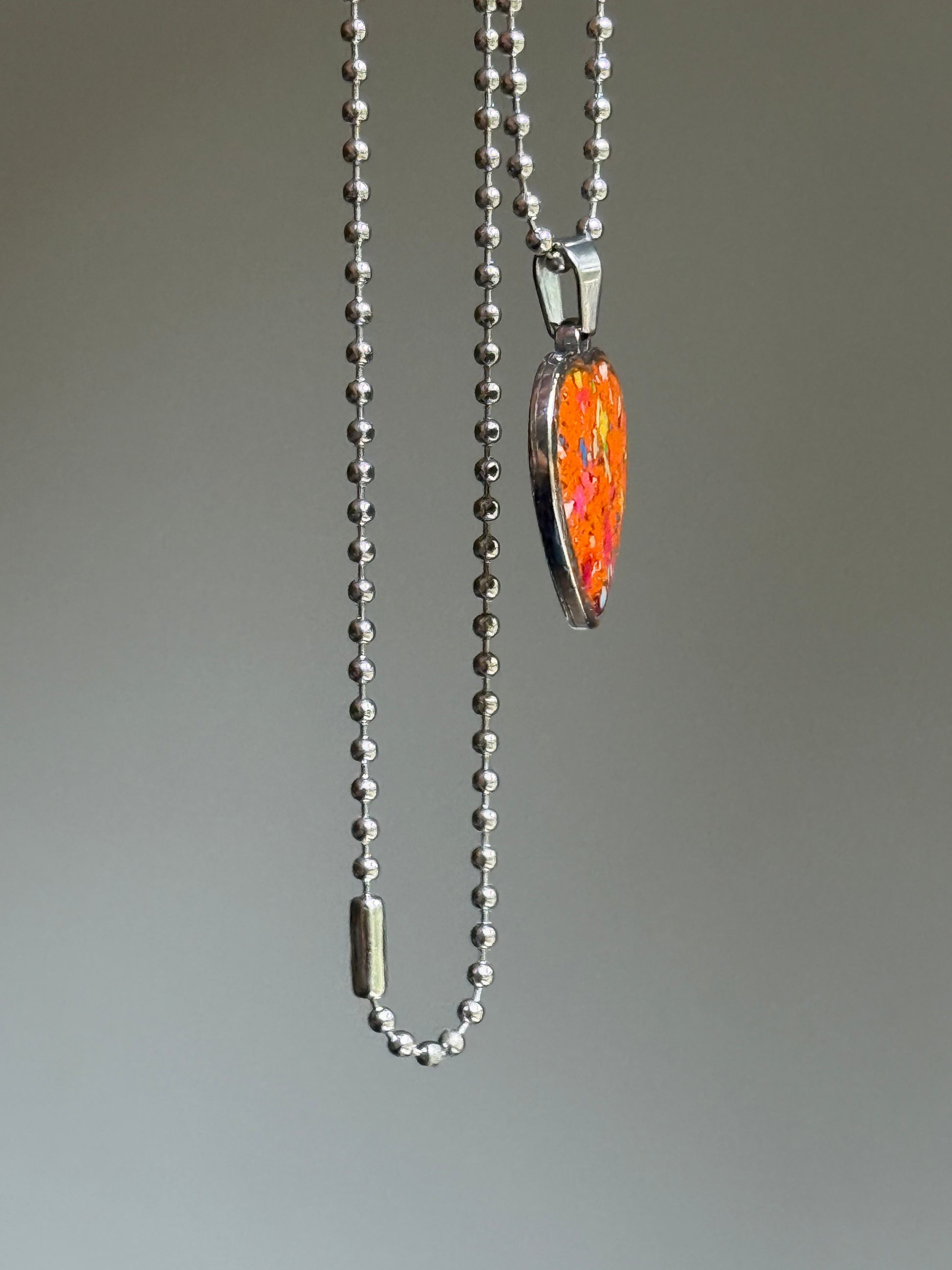 Side angle of a handcrafted heart pendant made with reclaimed crayons and hypoallergenic stainless steel. By Crayonfetti