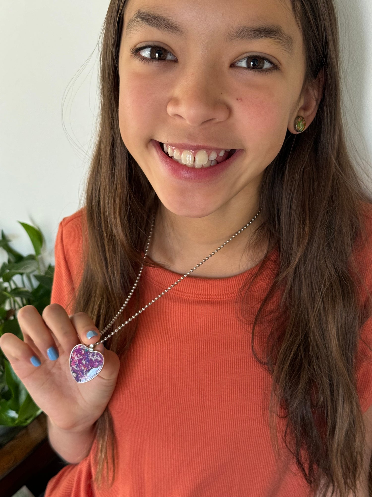 A girl wearing a orange top holding our purple heart-shaped pendant with a stainless steel chain.