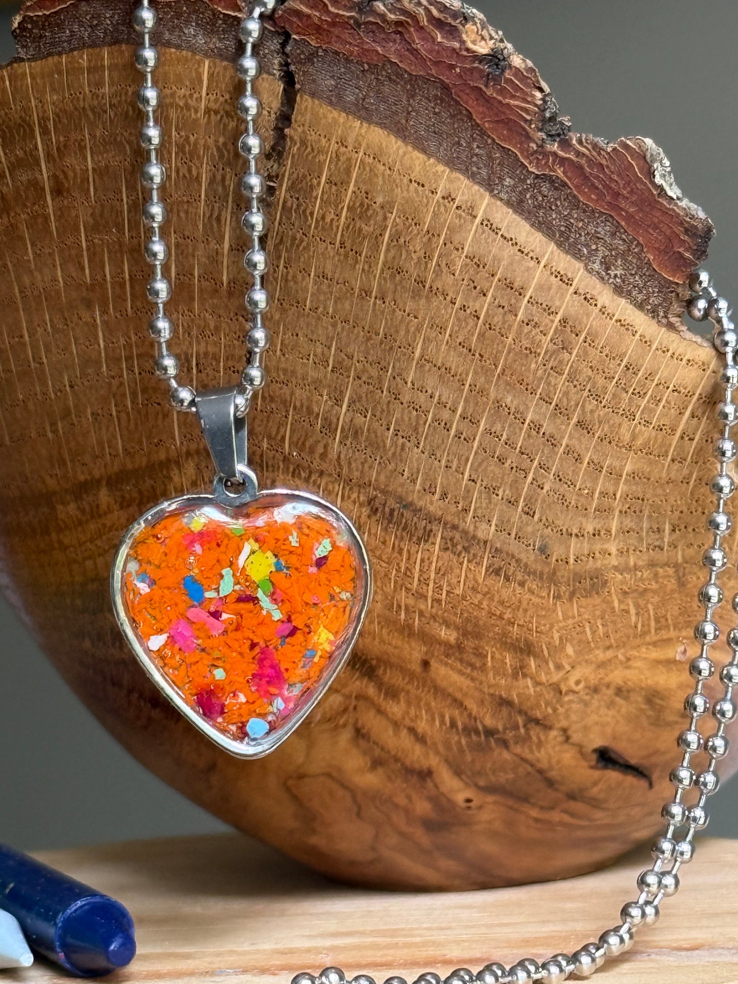 Handmade Sunburst State of Mind heart necklace made from reclaimed crayons in a stainless steel heart pendant with bold orange and colorful specks.