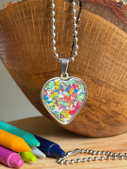 A stainless steel heart-shaped pendant necklace filled with multicolored crayon shavings.  Crayon jewelry by  Crayonfetti.