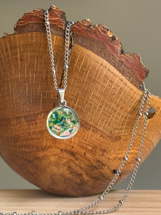 Dime-sized round pendant necklace with ocean blue green orange and pink resin art hanging over wooden bowl, bright gift for her. Crayon jewelry