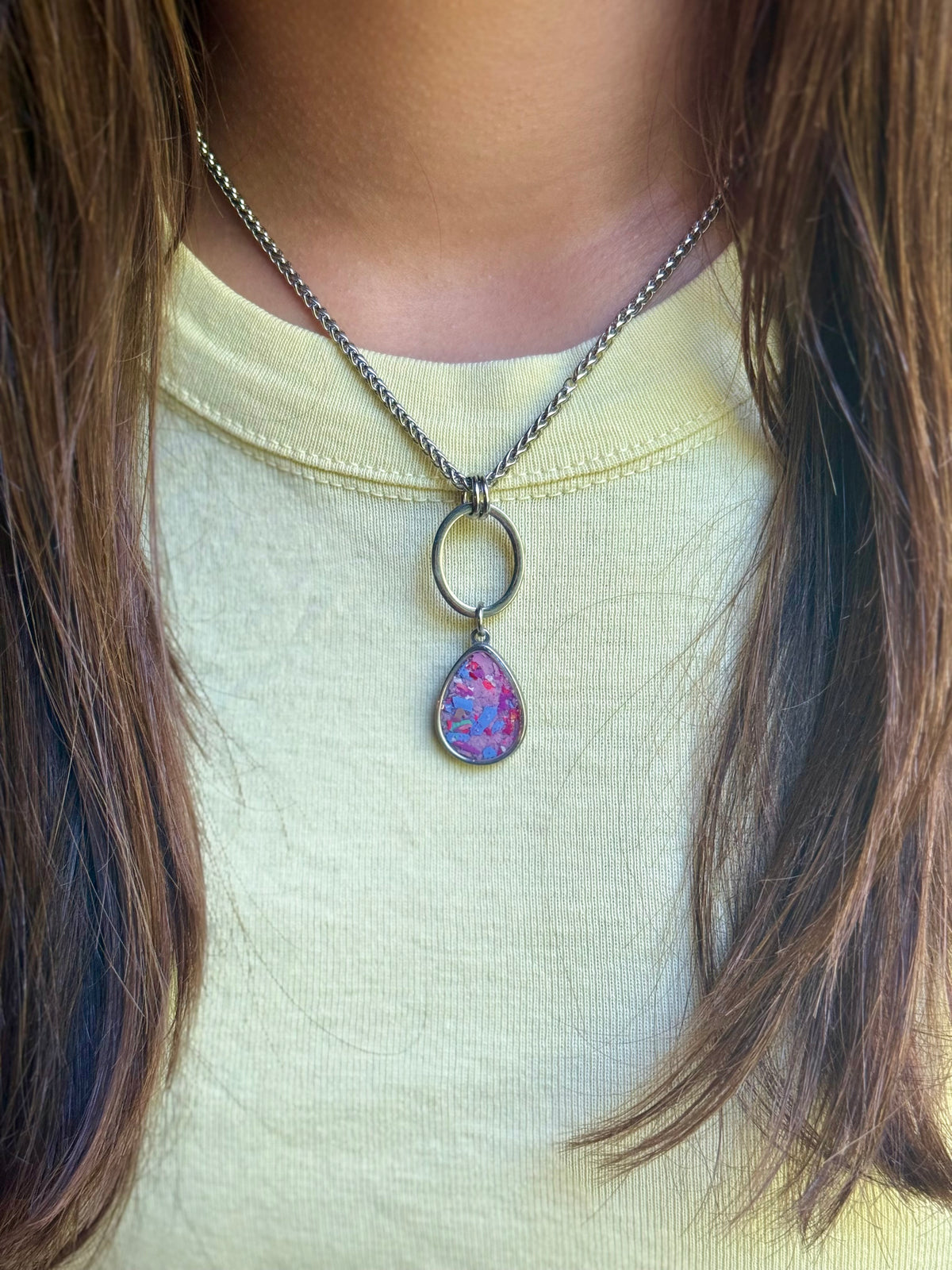 Model wearing the Carmen stainless steel pendant necklace filled with vibrant pink and lilac colorful detail.