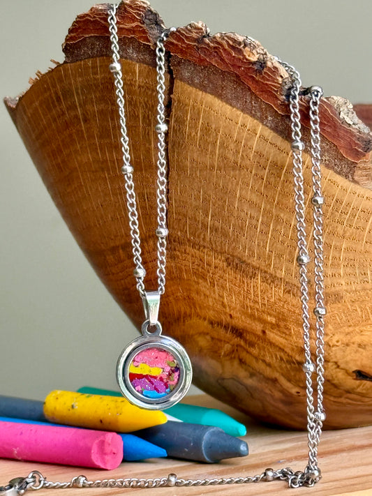 Close up of Artisan, round crayon jewelry pendant in stainless steel, unique art teacher gift.
