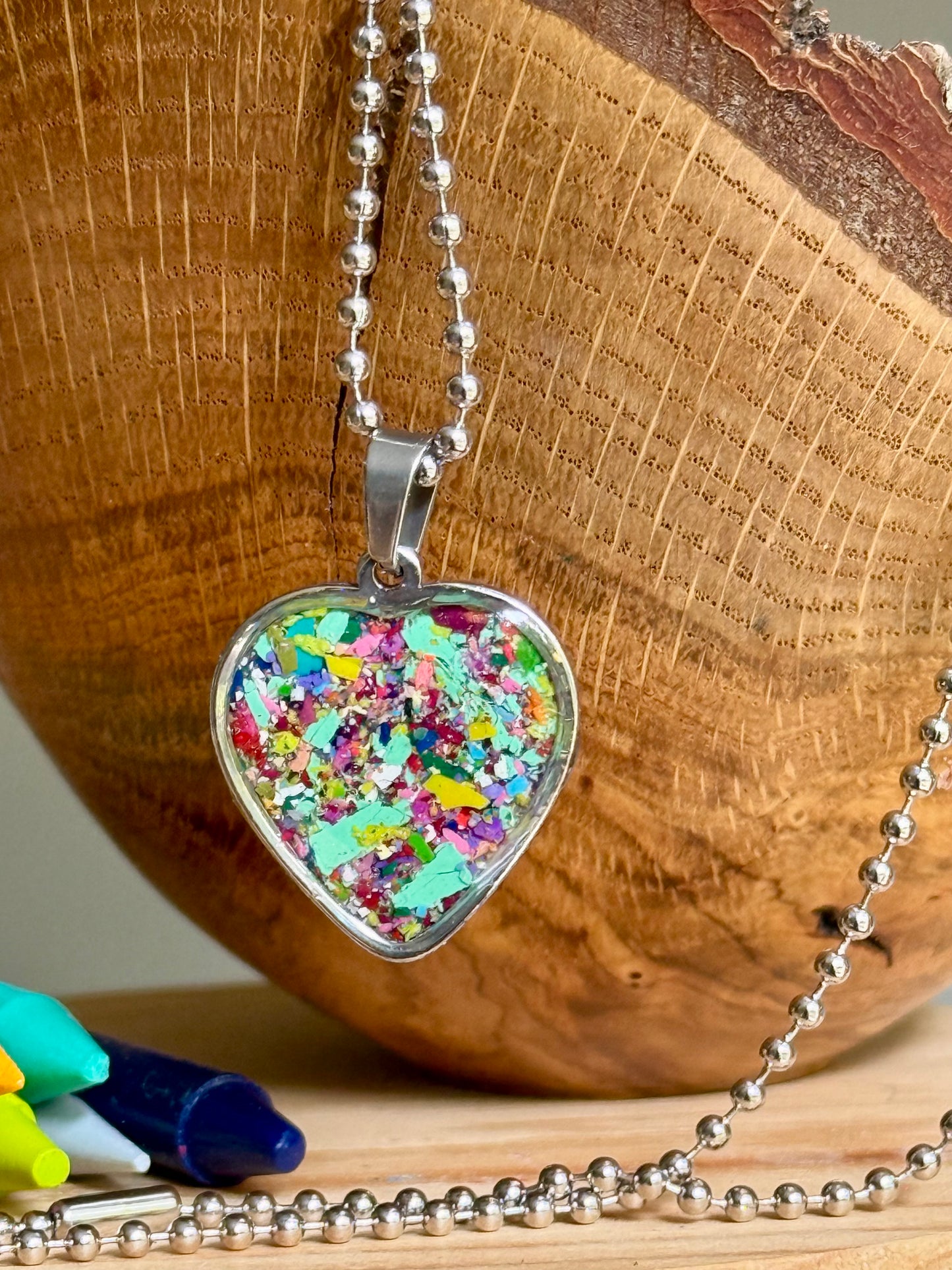 Handmade heart-shaped pendant filled with recycled crayon pieces in vibrant rainbow colors