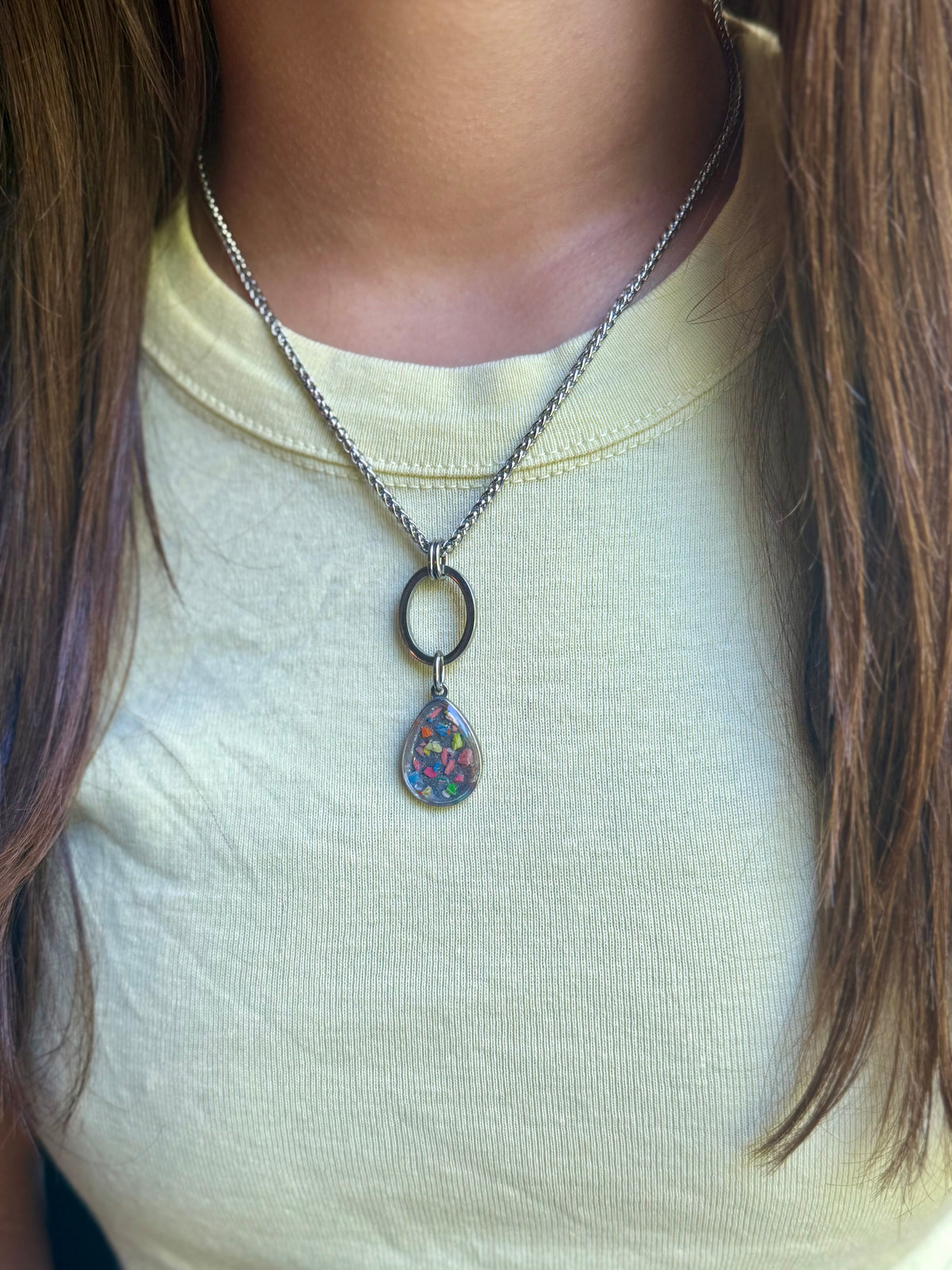 Model wearing the Pillar stainless steel geometric necklace featuring an open oval drop and 12mm round colorful resin and crayon base.