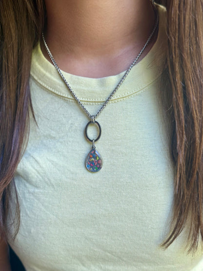 Model wearing the Pillar stainless steel geometric necklace featuring an open oval drop and 12mm round colorful resin and crayon base.